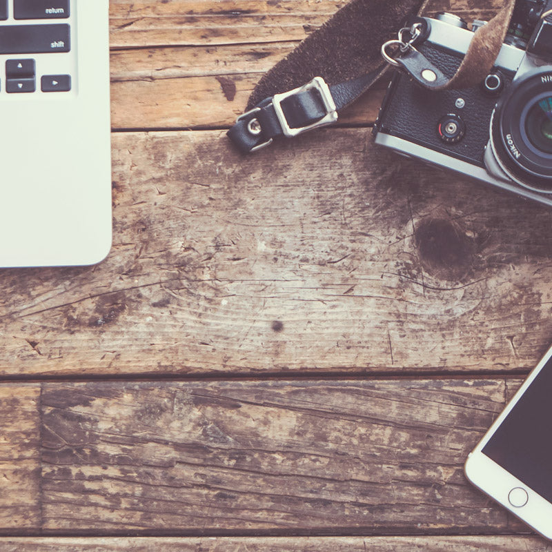 Desk full of creative supplies like an old camera, laptop and phone